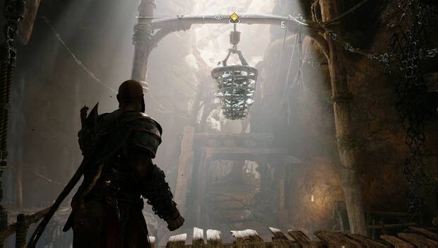 God of War: Ragnarok - En busca de Tyr: Kratos al borde de una plataforma de las minas. Frente a él, un punto de anclaje tiene una cesta de metal colgando. La cesta contiene mineral verde, como el que Atreus puede destruir con sus flechas