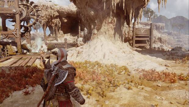 God of War: Ragnarok - En busca de Tyr: Kratos detenido en ua plataforma en el humedal de Svartalfheim. En el lado izquierdo se ve la cúpula de un géiser retirada, y Atreus contempla la rueda de agua justo encima. A la deecha, pasada una roca, hay unos tablones de madera por los que trepar