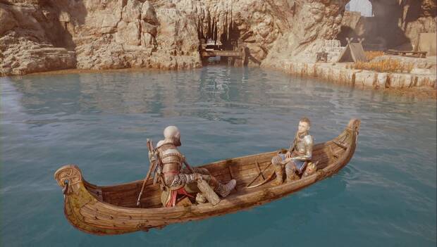 God of War: Ragnarok - En busca de Tyr: Kratos y Atreus está detenidos en la barca. Al fondo puede verse una tienda de campaña entre las hierbas, y una estructura de madera entre la roca y el agua que permite pasar por debajo en bote