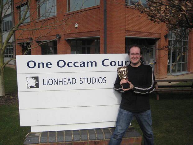 Serrano posa ante el cartel de Lionhead con el BAFTA conseguido por Fable 2en 2009.